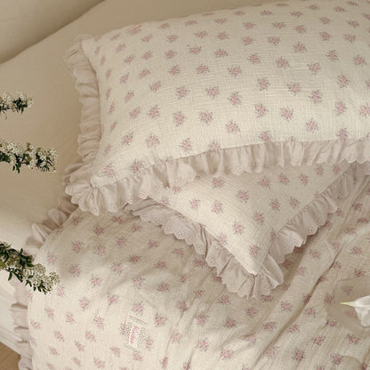 Matching pink floral pillows and comforter with ivory ruffled lace trim on a neutral bed