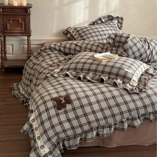 Plaid bedspread with ruffled edges and teddy bear applique on a bed in a bedroom setting.