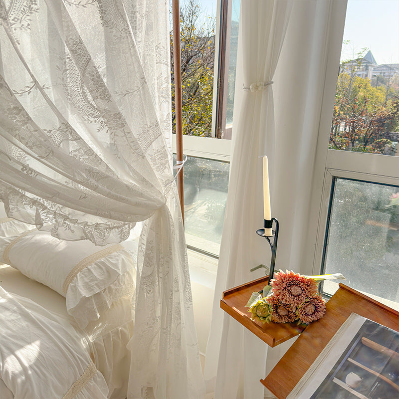 Sunny bedroom with white lace bed canopy, cotton bedding, flowers, and modern candle by window