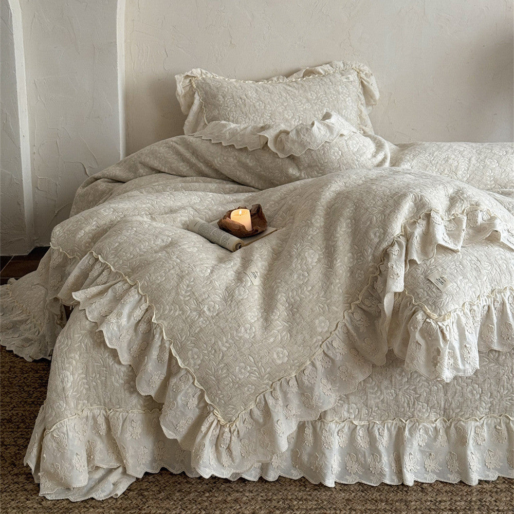Beige quilted linen cotton duvet cover and ruffled French bedspread ensemble draped over a bed. The set features a subtle floral quilt pattern and a beautiful scalloped ruffled border for a rustic, romantic bedroom look.