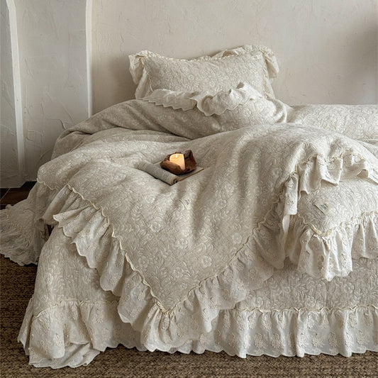 Beige quilted linen cotton duvet cover and ruffled French bedspread ensemble draped over a bed. The set features a subtle floral quilt pattern and a beautiful scalloped ruffled border for a rustic, romantic bedroom look.