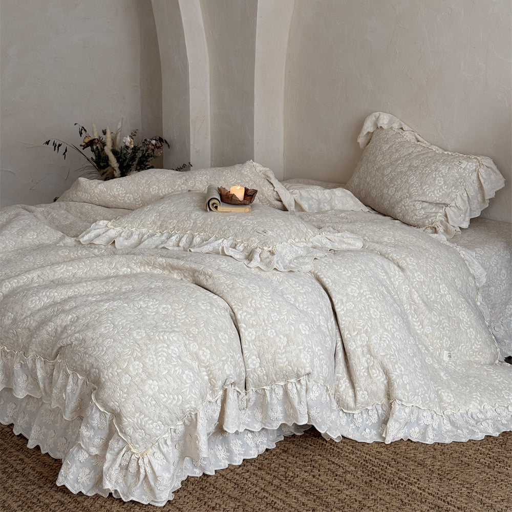 A complete look at the beige quilted linen cotton duvet cover set on a large bed in a bright, arched-nook room. The French-style bedspread has elegant, voluminous ruffle edges near the floor.