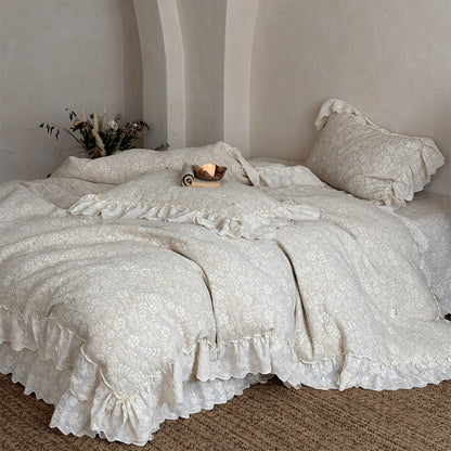 A complete look at the beige quilted linen cotton duvet cover set on a large bed in a bright, arched-nook room. The French-style bedspread has elegant, voluminous ruffle edges near the floor.