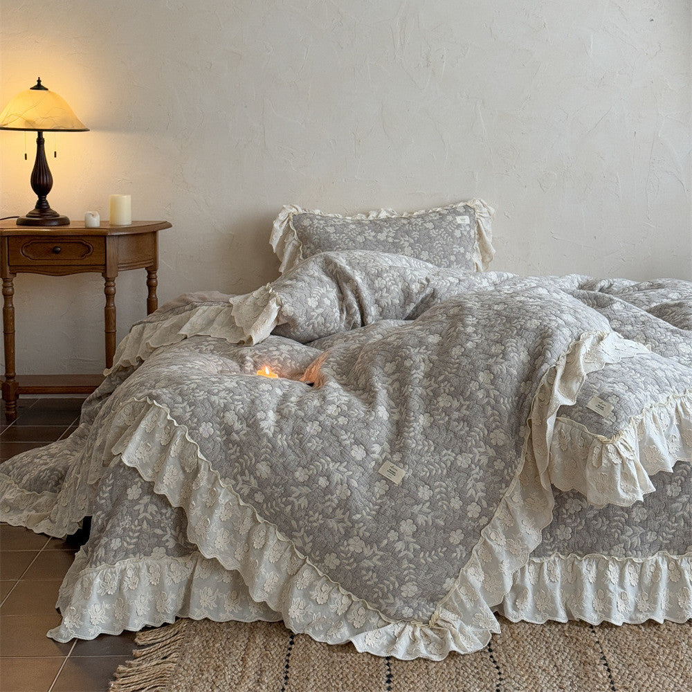 Full view of the bed featuring the grey quilted linen cotton duvet cover and coordinating French ruffled bedspread, showing the soft, textured floral print and the contrasting cream lace ruffle detail.