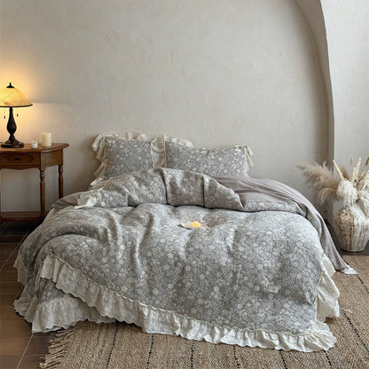 Grey quilted linen cotton duvet cover and ruffled lace bedspread on a bed in a cozy, bright room. The matching pillow shams are visible, showcasing the bedding's French rustic style with the contrasting white ruffle.