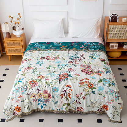 Reversible botanical cotton throw blanket showing ivory floral side on a white bed