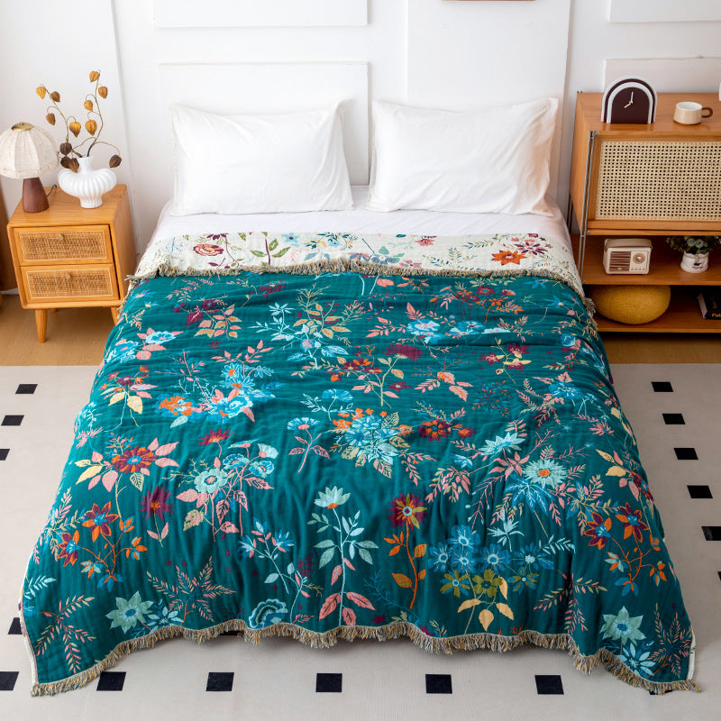 Deep teal botanical cotton throw blanket with colorful floral pattern and fringe on bed