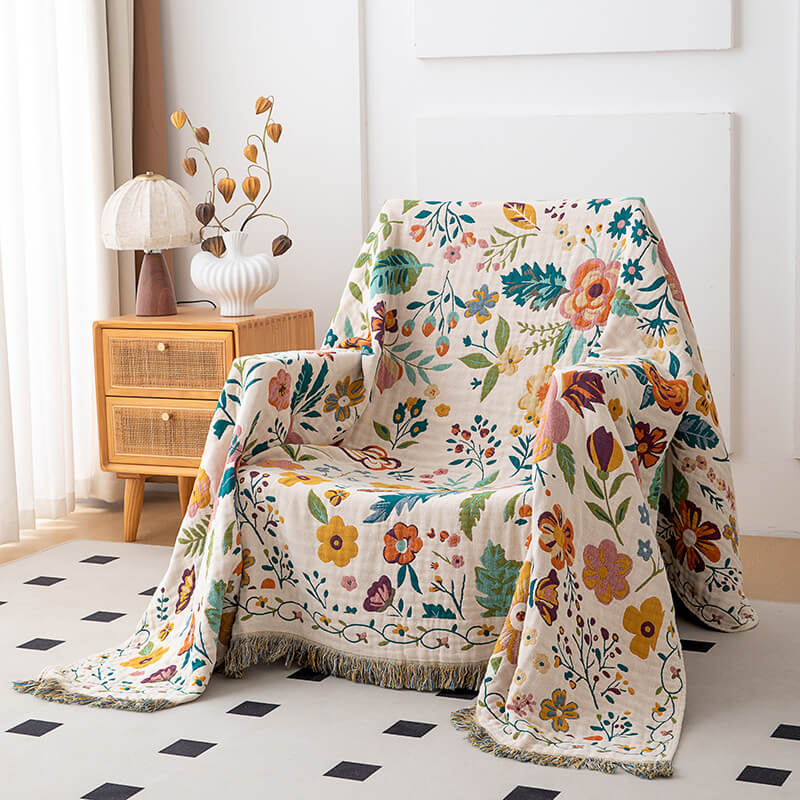 Ivory floral cotton throw blanket with fringe draped over an accent chair