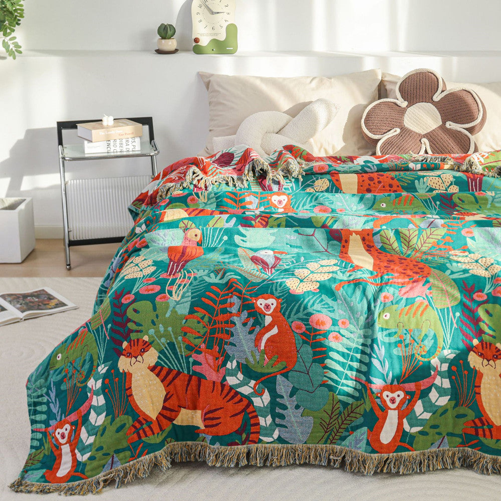 Reversible Jungle Animal Cotton Jacquard Throw draped over a bed corner, highlighting the premium cotton weave, detailed tassel edges, and vibrant tropical print against neutral bedding.