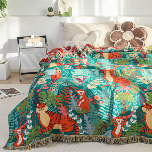 Reversible Jungle Animal Cotton Jacquard Throw draped over a bed corner, highlighting the premium cotton weave, detailed tassel edges, and vibrant tropical print against neutral bedding.