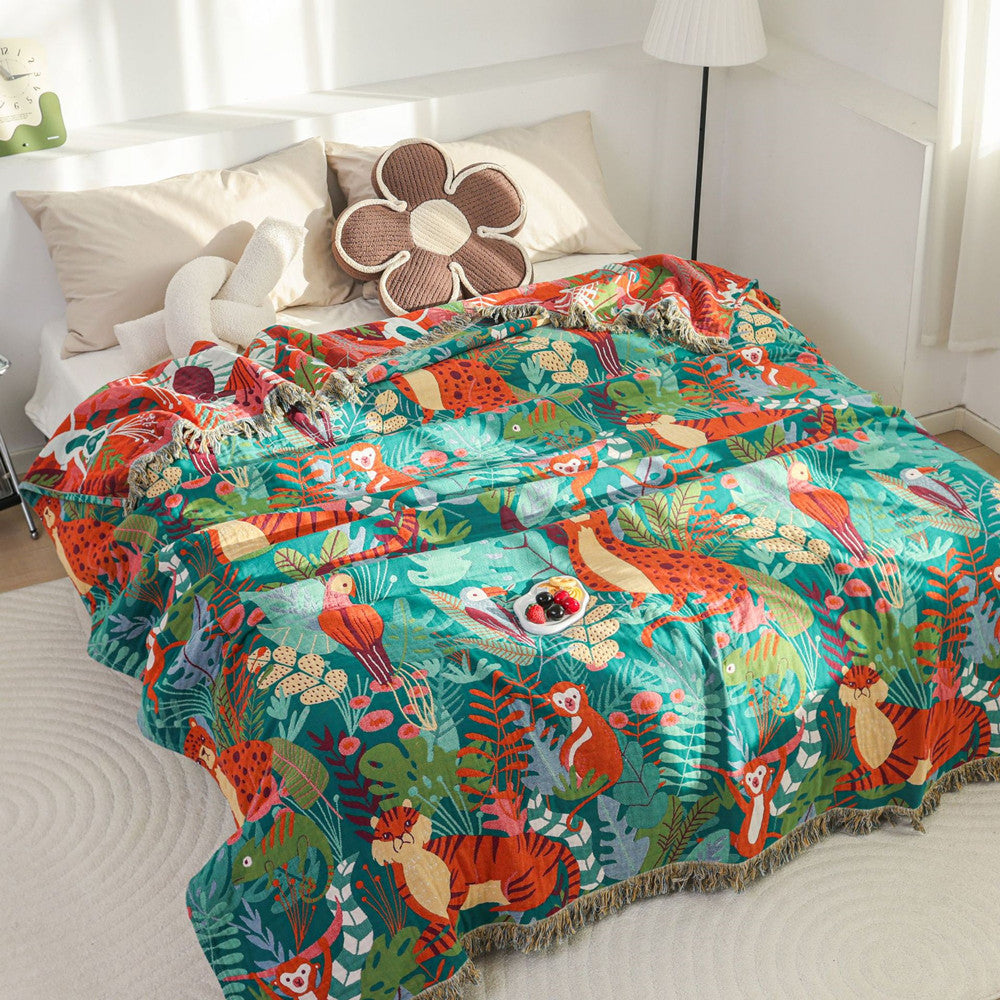 Large Jungle Animal Cotton Jacquard Throw Blanket spread flat on a bed, showcasing the full size of the reversible design with a folded corner revealing the warm-toned underside.