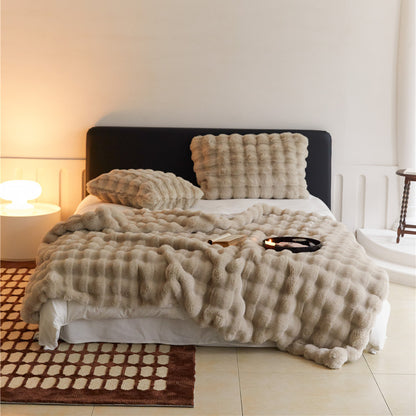 A warm, tan-colored faux rabbit fur throw blanket with a puffy grid texture, covering a bed with a matching pillow.