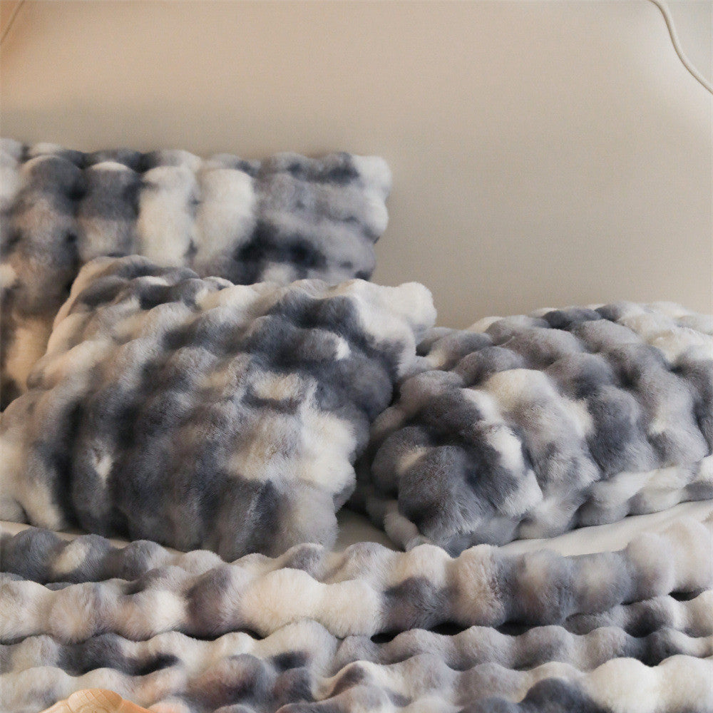 A detailed close-up of a gray and white tie-dye patterned faux rabbit fur blanket and matching pillow with a fluffy, bubbly texture.