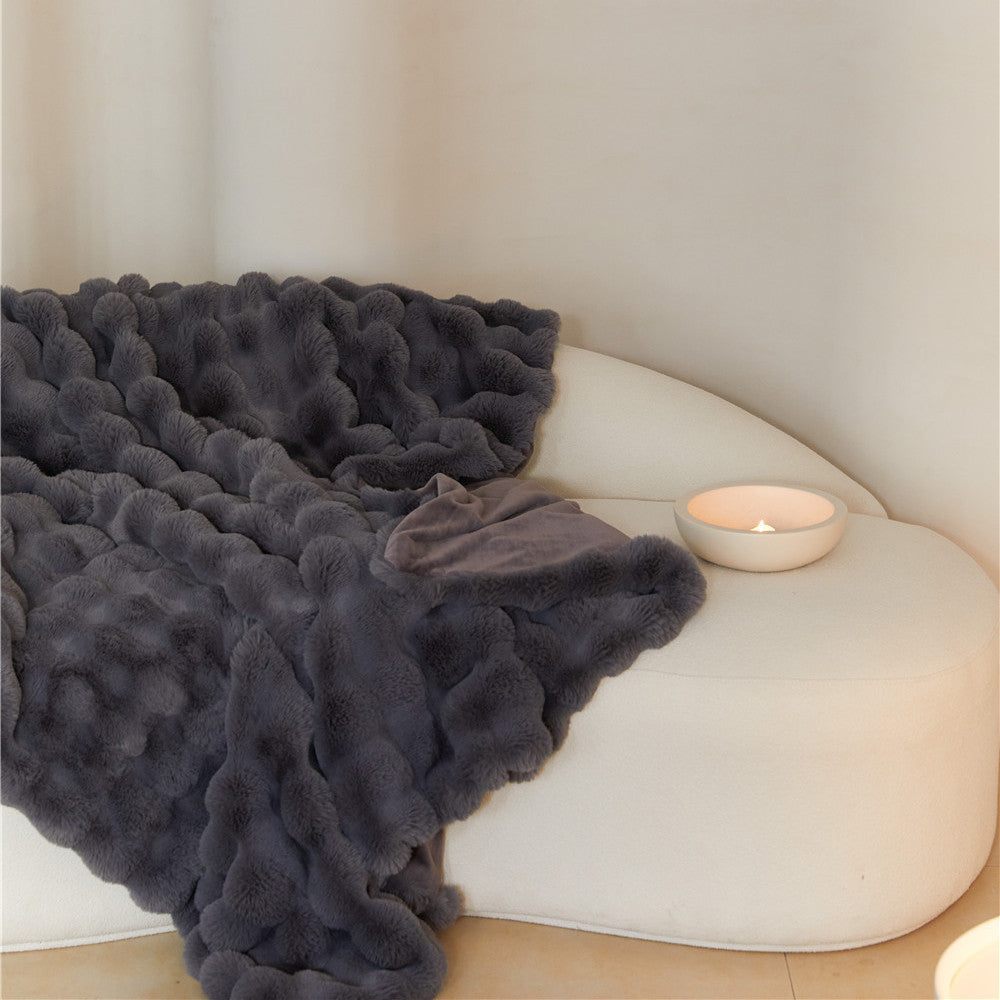 A close-up of a Charcoal faux rabbit fur blanket with a bubble pattern, casually draped over a cream-colored armchair.