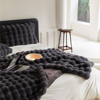 A Charcoal faux rabbit fur throw blanket with a bubble texture, draped over a bed with a matching pillow.