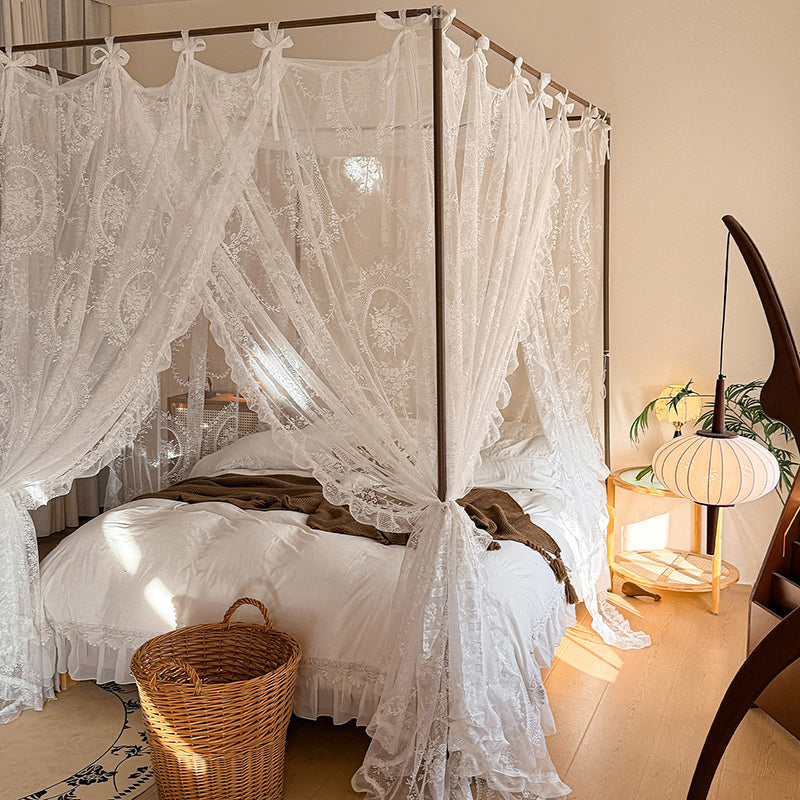 Romantic lace canopy curtains on a four-poster bed with white bedding in a cozy bedroom