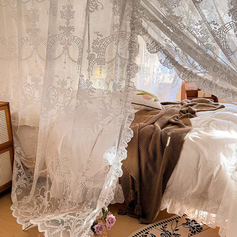 Lace curtains in a bedroom with a bed and chair.