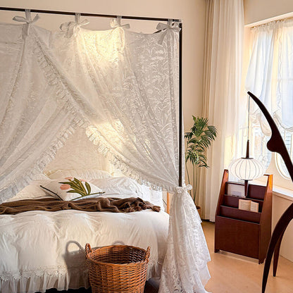 Bedroom with a canopy bed draped with white lace curtains, a plant, and a wooden side table.