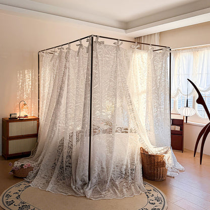 Canopy bed with lace curtains in a room with wooden floors and a window.