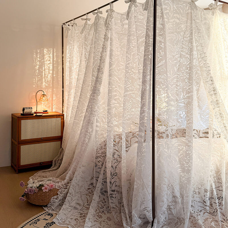 Lace curtains in a room with a wooden cabinet and lamp.