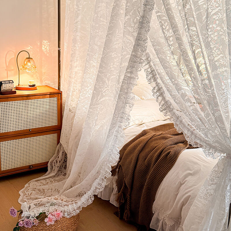 Bedroom with lace curtains, wooden dresser, and floral arrangement.