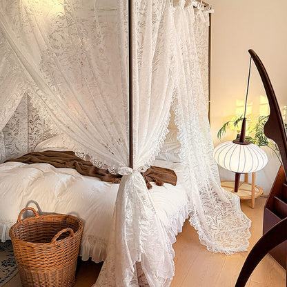 Bedroom with a canopy bed made of lace curtains, a basket on the floor, and a lamp in the background.