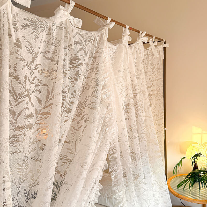 White lace curtains hanging on a wooden rod with a neutral background.