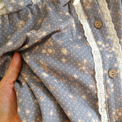 Blue cotton pajama set with floral print, lace trim, and wooden buttons, held by hand