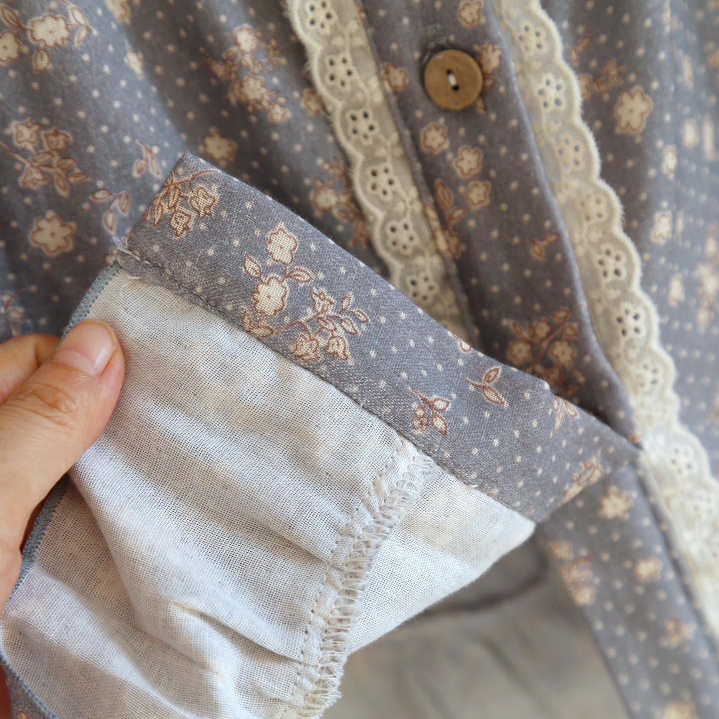 Hand holding floral ruffled cotton pajama with lace trim and wooden button detail