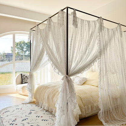 Romantic white lace ruffled canopy bed curtains in a sunny, cozy bedroom with natural light
