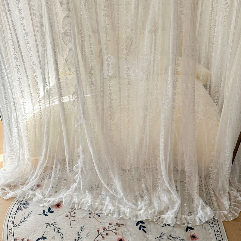 White lace canopy bed curtains with ruffles over a cozy bed and floral rug