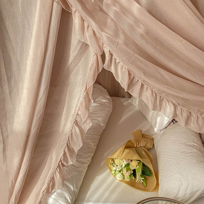 Romantic ruffled canopy curtains over a four-poster bed with white cotton bedding and a bouquet
