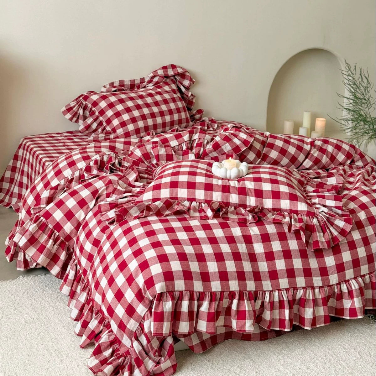 Red checkered muslin bedding set with ruffles and pillows, giving a vintage feel.