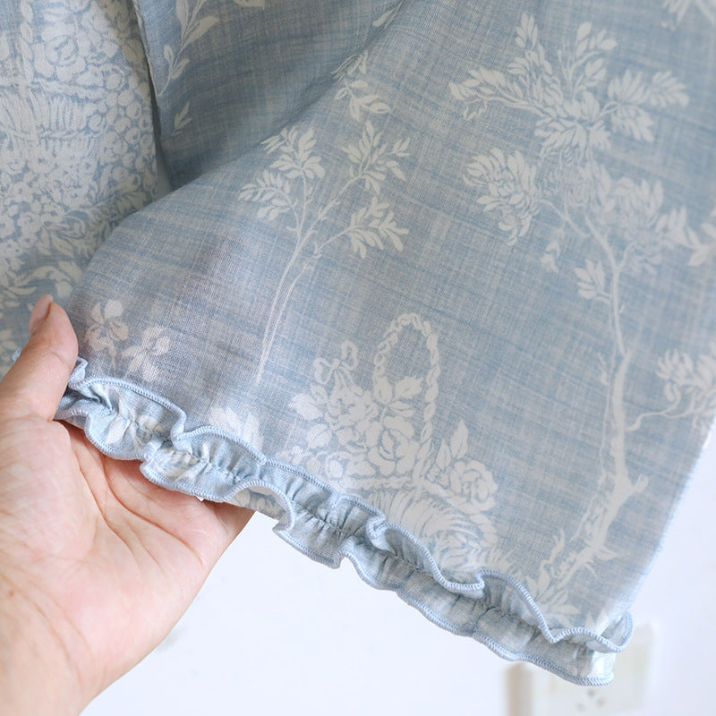 Hand holding light blue cotton pajama fabric with white floral print and ruffled edge