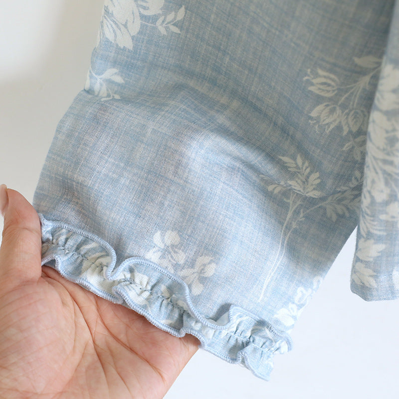 Hand holding soft blue cotton pajama sleeve with white floral print and ruffled trim