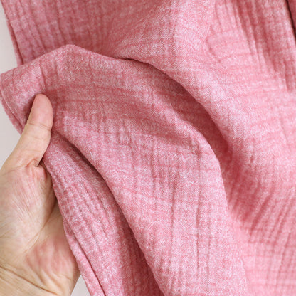 Hand holding soft pink cotton gauze fabric, showing texture and lightweight material