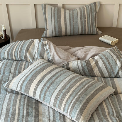 Striped cotton gauze bedding set with blue, gray, and white tones on a brown fitted sheet, book on side table