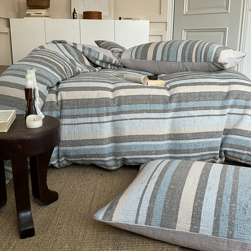 Striped cotton gauze bedding set with blue, gray, and beige tones on cozy bed with matching pillows