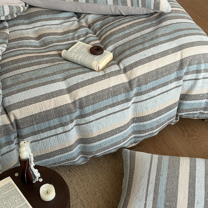 Striped cotton gauze bedding set in blue, gray, and cream on bed with open book and candles