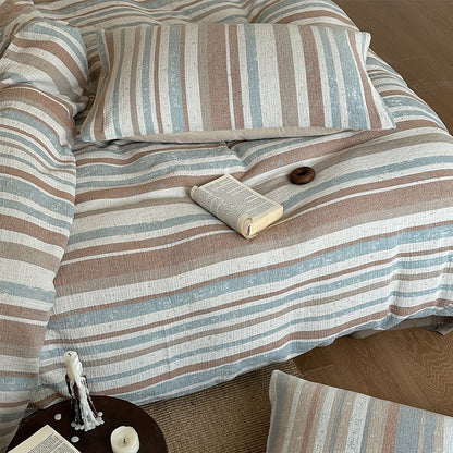 Natural striped cotton gauze bedding set in muted earth tones with cozy pillow and book