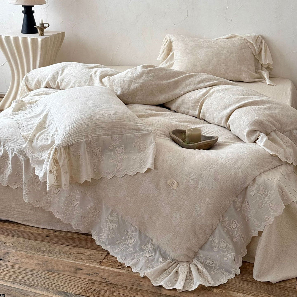Textured beige linen cotton bedding set with embroidered trim, pillows, and duvet on wooden floor