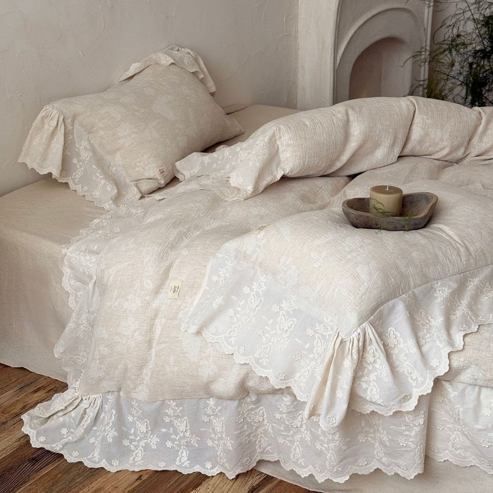 Textured linen cotton bedding set with embroidered floral trim on bed with wooden floor.