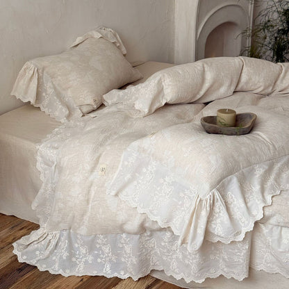 Textured linen cotton bedding set with embroidered floral trim on bed with wooden floor.