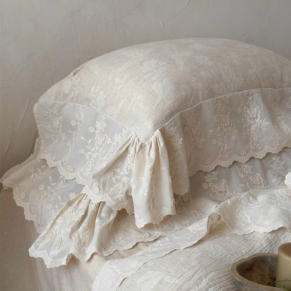 Beige linen pillow with delicate white embroidered lace trim featuring floral and butterfly patterns