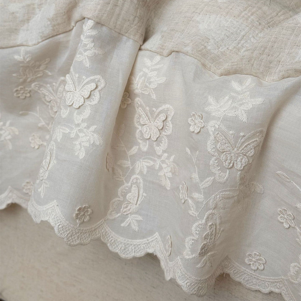 Close-up of textured linen cotton fabric with embroidered butterfly and floral trim in neutral tones