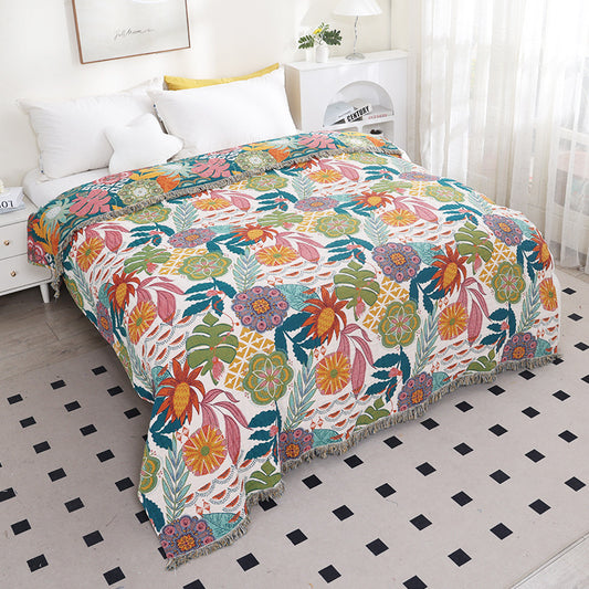 Tropical floral cotton throw blanket with fringe styled across a white bed