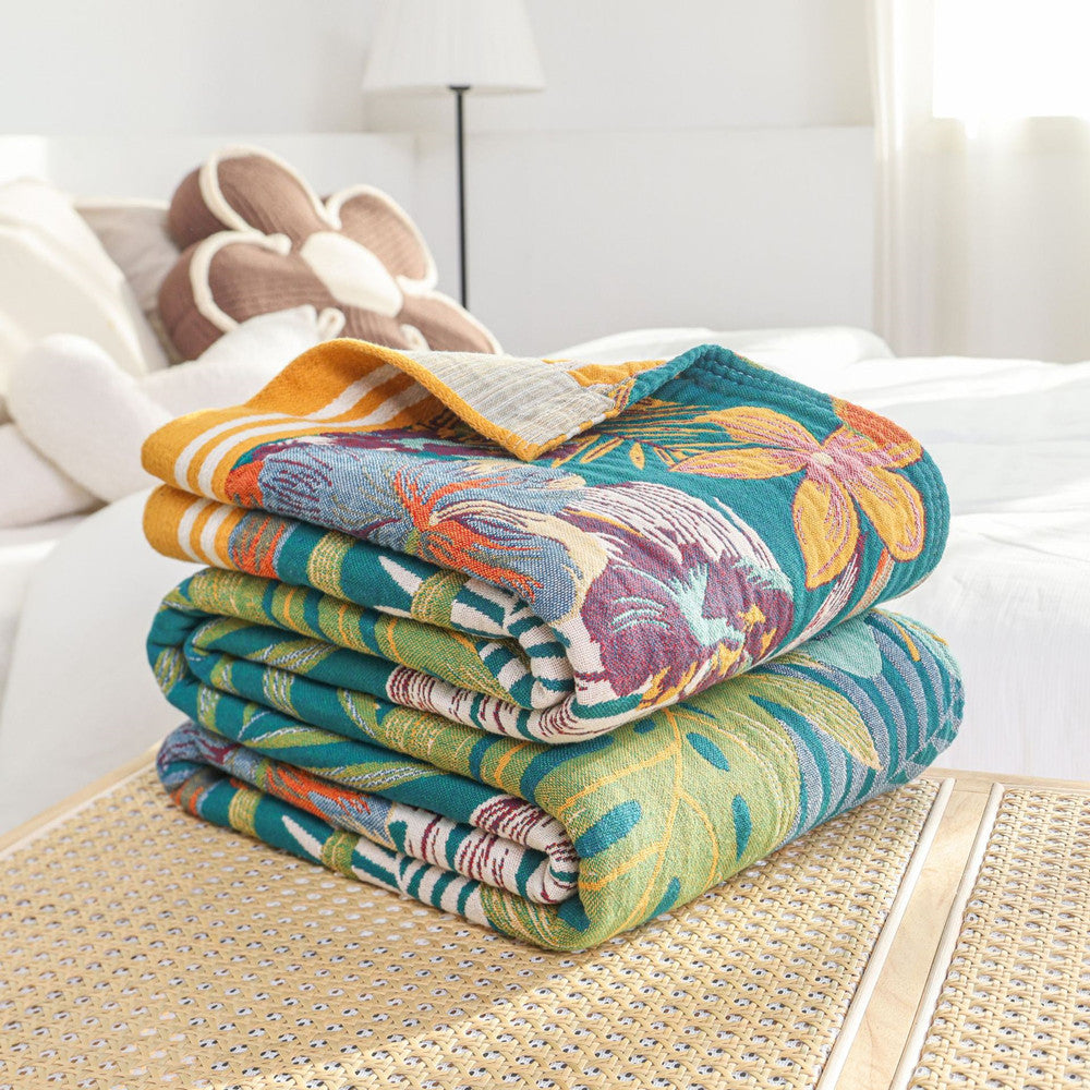 Folded stack of the Tropical Paradise Cotton Throw Blanket on a rattan table, revealing the thick woven cotton texture, hem details, and reversible color layers.