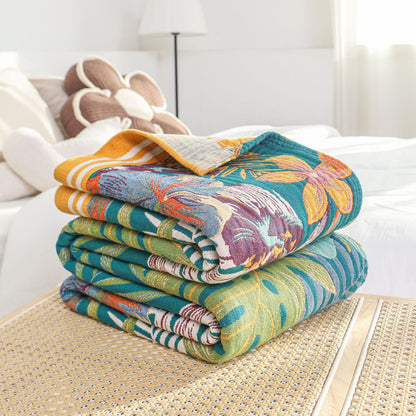 Folded stack of the Tropical Paradise Cotton Throw Blanket on a rattan table, revealing the thick woven cotton texture, hem details, and reversible color layers.
