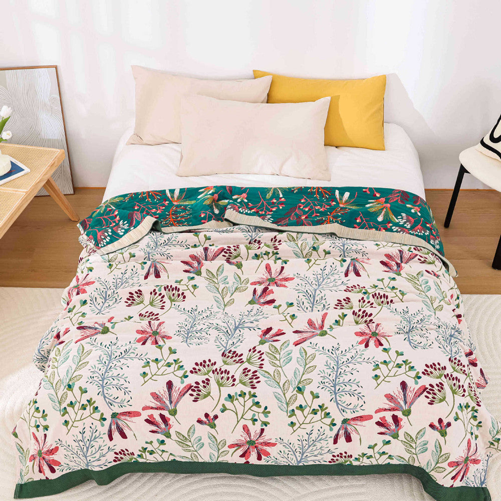 A bed styled with a cream wildflower-patterned cotton throw blanket and a dark green reversible top edge.