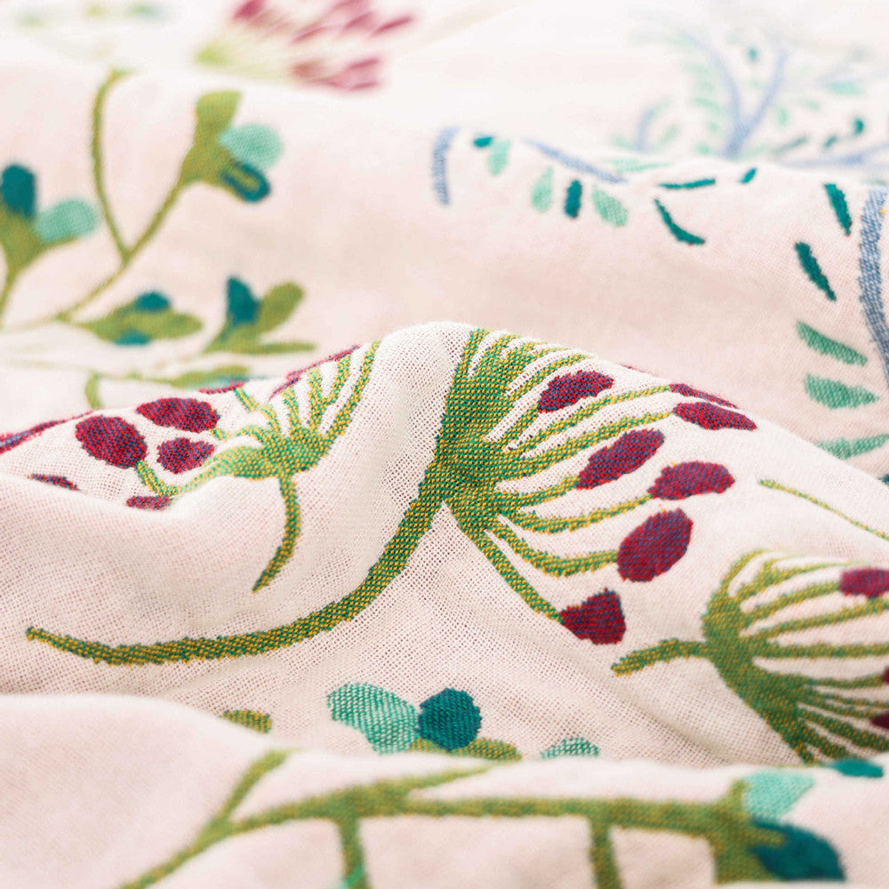 Close-up of the cream side of a cotton throw blanket featuring woven berry and leaf botanical illustrations in red and green.